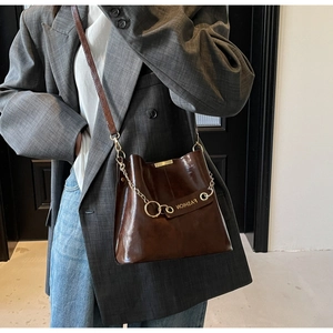 Detail of dark brown bucket bag with gold fashion lettering and chain on suit model