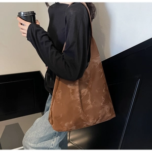 Dettaglio di una grande borsa tote marrone tie-dye indossata da una modella su sfondo moderno