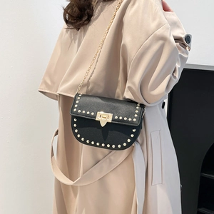 Sac besace noir à rivets et chaîne dorée porté sur un trench-coat beige