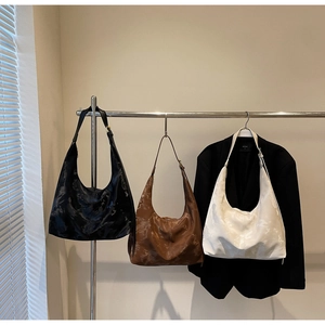 Three minimalist crescent tote bags in black, brown and beige hanging on a metal rack