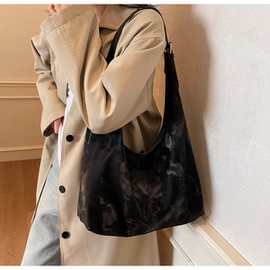Detail of black large hobo bag with marble texture and gold hardware on a beige coat