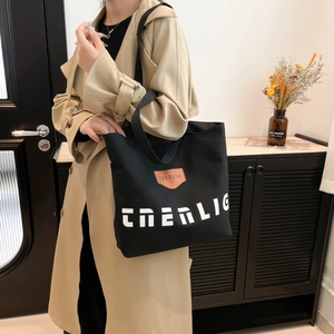 Minimalist black canvas tote bag with brown leather patch and shoulder strap for women