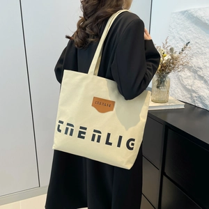 Minimalist canvas tote bag with CNERLIC text and brown leather tag on a female model