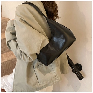 Detail of a black glossy crescent shoulder bag showing minimalist texture and silhouette