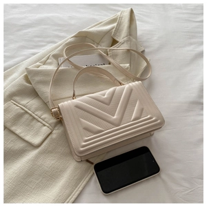 Close-up of cream quilted crossbody bag with phone for size reference on white blazer
