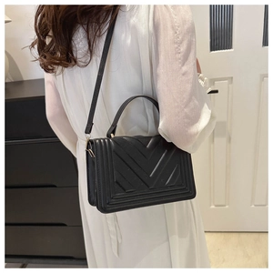 Detail of black V-quilted handbag with gold hardware and elegant top handle strap
