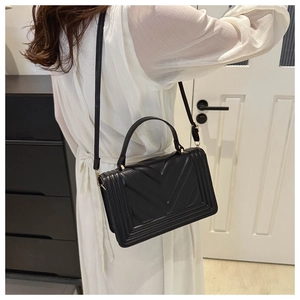 Detail of black quilted leather shoulder bag featuring V-shaped embossed patterns and gold hardware