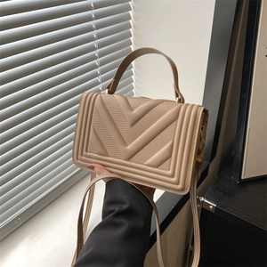 Detailed view of beige crossbody bag with V-shaped quilting and gold hardware accents
