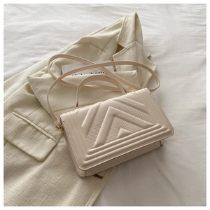 Detail of beige textured handbag showing V-shaped embossed leather on a blazer