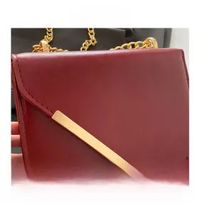 Detail of burgundy leather shoulder bag with gold metal bar and chain strap