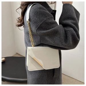 Detail of elegant cream shoulder bag with gold chain strap and metallic bar accent