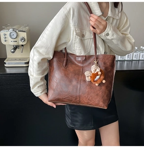 Détail d'un sac cabas marron vintage en cuir huilé avec un pendentif monstre en peluche