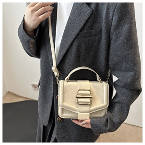 Detail of cream white leather handbag with gold metal buckle on charcoal blazer