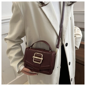 Detail of vintage burgundy leather handbag featuring a prominent gold rectangular metal buckle