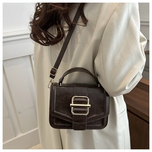 Close-up of a dark coffee crossbody bag with a golden rectangular buckle on a white blazer