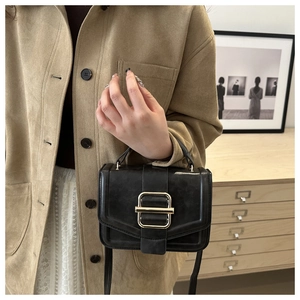 Detail of minimalist black crossbody bag with gold buckle on a stylish model outfit