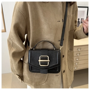 Detail of a minimalist black crossbody bag featuring a matte finish and gold metal buckle