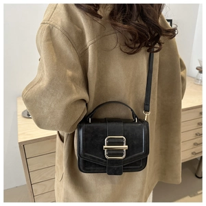 Model wearing a black retro square crossbody bag with a gold buckle and tan coat