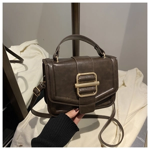 Detail of a vintage dark brown PU leather handbag with a large square gold metal buckle