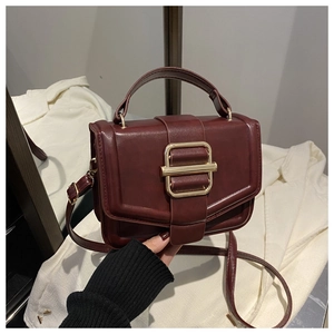 Detail of a dark red commuter handbag with large gold buckle and smooth leather finish