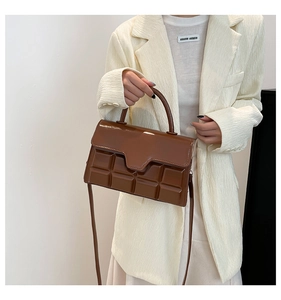 Detail of a brown chocolate-patterned patent leather handbag with top handle and strap