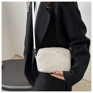 Detail of white woven texture camera bag with gold hardware worn by model over black coat