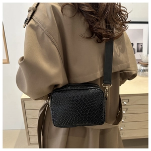 Detail of black woven crossbody camera bag with wide strap on a khaki trench coat