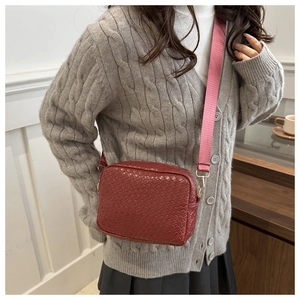 Detail of burgundy crossbody bag with woven texture and pink strap on grey sweater