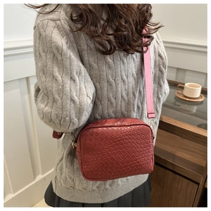 Detail of woven texture small square bag with contrasting pink strap in a lifestyle setting