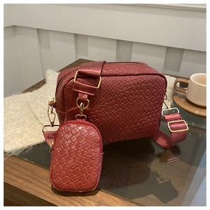 Close-up of red woven camera bag with detachable mini pouch and gold hardware on wood