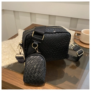 Detail of black woven texture crossbody bag with detachable mini pouch on wood surface