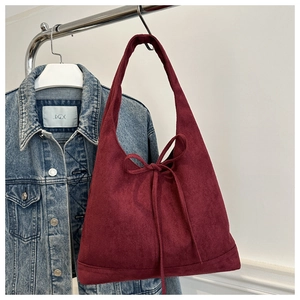 Detail of burgundy suede tote bag featuring a decorative bow on a metal hanger