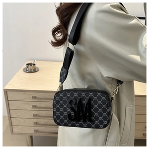 Close-up of black crossbody bag with wide strap, SM logo, and gold metal hardware detail