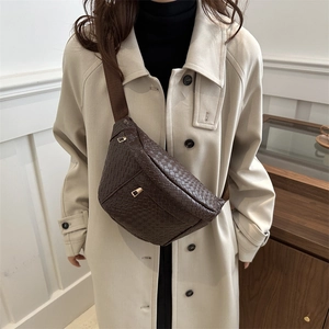 Deep brown woven leather crossbody bag with adjustable strap worn by model in a beige coat
