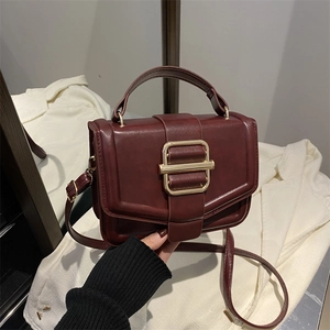 Détail du sac à main en cuir bordeaux avec boucle rectangulaire dorée et poignée ronde