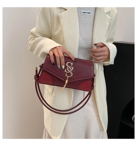 Detail of burgundy leather shoulder bag with gold tassel logo on beige blazer