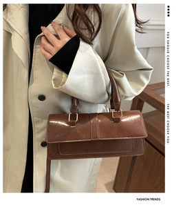 Detail of glossy coffee brown baguette bag with gold metal hardware and smooth finish