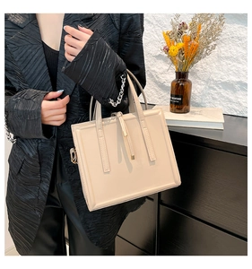 Detail view of a beige minimalist square handbag with top handles and leather charm decoration