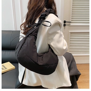 Detalle del bolso de nube acolchado negro con correa fruncida sobre blazer blanco