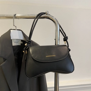 Detail of matte black shoulder bag featuring gold text and knotted strap design