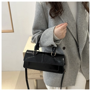 Detail of a black patent leather shoulder bag on a model wearing a grey tweed blazer