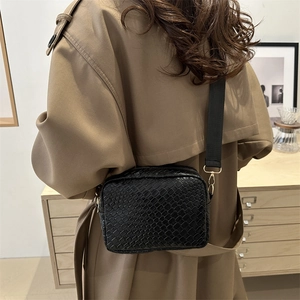 Fashionable black woven crossbody camera bag with wide strap on khaki trench coat