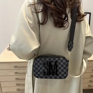 Modern crossbody camera bag in dark monogram leather with broad strap shown on a model