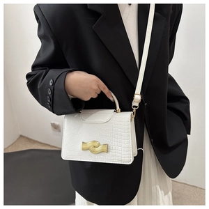 Détail d'un sac carré blanc à motif crocodile avec fermoir doré sur une veste noire