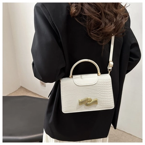 Sac blanc motif crocodile avec poignée dorée et fermoir vague porté sur une veste noire