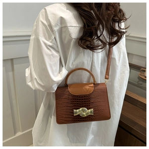 Brown crocodile embossed leather handbag with wave buckle shown on model side profile