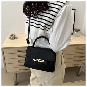 Detail of a vintage black leather handbag with a gold lock clasp on a shoulder strap