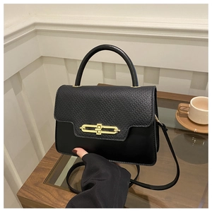 Detail of black crossbody bag with crocodile texture flap and gold chain twist lock