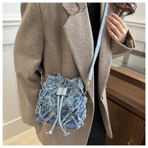 Close-up of blue denim bucket bag with floral fringe texture and drawstring detail