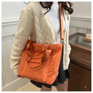 Vibrant orange nylon tote bag detail featuring wide fabric handles and a detachable strap